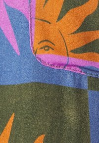 Kolorowa tkanina z odważnym słońcem i abstrakcyjnymi wzorami w odcieniach pomarańczowym, różowym i zielonym. Teksturowana powierzchnia z przeszytym fioletowym szwem.