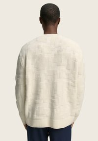 Strickpullover in Creme mit geometrischem Muster, ausgestattet mit gerippten Bündchen und Saum. Der Stoff wirkt weich und gestrickt.