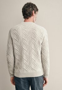 Hellgrauer gestrickter Pullover mit einem strukturierten, geometrischen Muster sowie gerippten Bündchen und Saum. Die Rückseite ist mit einem Kreuzdesign verziert.