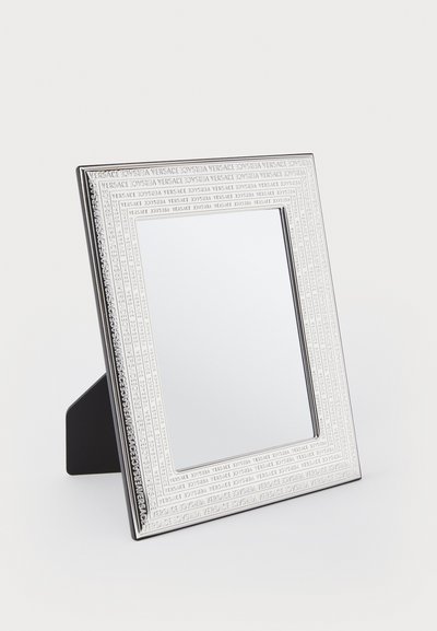 Kvadratiskt spegel med en silverfärgad, graverad ram som visar upprepad text. Svart ställning på baksidan för stöd. Slät, reflekterande yta.