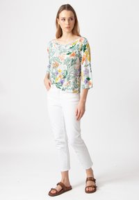 Bloemenprint, lichtgewicht top met 3/4 mouwen in pastelkleuren; gecombineerd met witte slim-fit broeken en bruine sandalen met een gespsluiting.