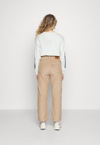 Chemise à manches longues bleu clair associée à un pantalon large en velours côtelé beige. La chemise a des manches à motifs et le pantalon présente des poches arrière.