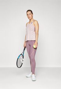 Tenis odijelo koje se sastoji od svijetloplavog topa bez rukava s mrežastim detaljima i kontrastnim narančastim rubovima, u kombinaciji s uskim lavandastim legginama i bijelim cipelama.