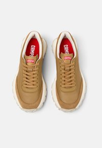 Sneakers in pelle marrone con inserti testurizzati, suole bianche e lacci prominenti. La fodera interna rossa presenta il nome del marchio "CAMPER."