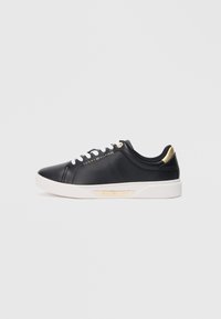 Mustmust musta nahk sneaker valge tallaga ja valgete paeltega. Kuldne aktsent kanna ja logo peal. Ümar varvas ja minimalistik disain.