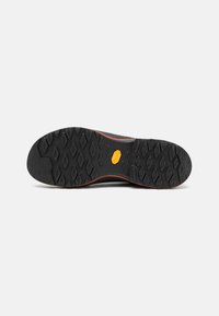 Suola nera di scarpa con superficie in gomma testurizzata, caratterizzata da battistrada esagonale e un logo arancione centrale per una migliore aderenza e durata.