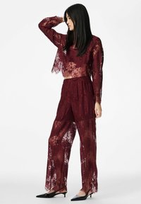 Vīnsarkans mežģīņu divdaļīgs komplekts ar īsu topu ar garām piedurknēm un augstiem, platiem biksēm ar smalkām ziedu rakstiem.