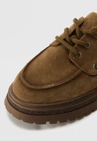 Braune Wildlederschuhe mit Schnürdesign, runder Zehenform und einer dicken strukturierten Sohle mit einem kontrastierenden braunen Akzent.