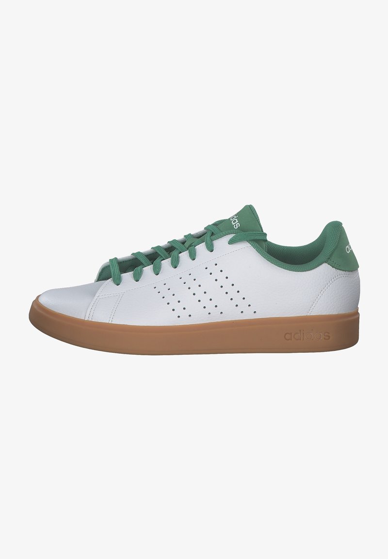 Zapatilla blanca con acentos verdes, hecha de cuero suave, con perforaciones en el costado y una suela de goma marrón. Cintas en color verde a juego.