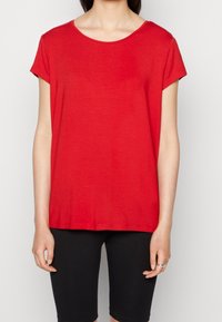 Rød, kortærmet t-shirt med rund halsudskæring, lavet af blødt stof, afslappet pasform, ensfarvet design, båret over sorte shorts.