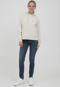 Helle graue Kapuzen sweatshirt mit einer Fronttasche und Kordelzug, kombiniert mit dunkelblauen Skinny-Jeans und weißen Sneakern.