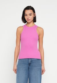 Εφαρμοστό ριμπ αμάνικο τοπ σε φωτεινό ροζ με στρογγυλή λαιμόκοψη και σχεδιασμό χωρίς μανίκια, συνδυασμένο με ανοιχτό μπλε παντελόνι με φαρδιά πόδια.