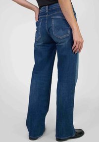 Jean en denim bleu à jambes larges et taille haute, avec deux poches arrière et un motif de couture subtil. Tissu lisse avec une teinte classique.