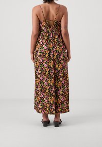 Blommig maxi-klänning med svart bakgrund och färgglada rosa, gula och orange blommor. Axellös design på ryggen med volangdetaljer.