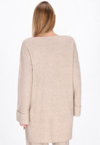 Maglione beige lavorato a maglia con una vestibilità ampia, maniche lunghe e polsini arrotolati. Presenta un motivo testurizzato e un orlo dritto.