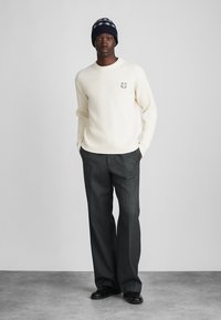 Kremveida ribota džemperis ar mazu izšūtu lāci, apvienots ar tumši pelēkām pieguļošām biksēm un melnām kurpēm, papildināts ar tumši zilu cepuri.