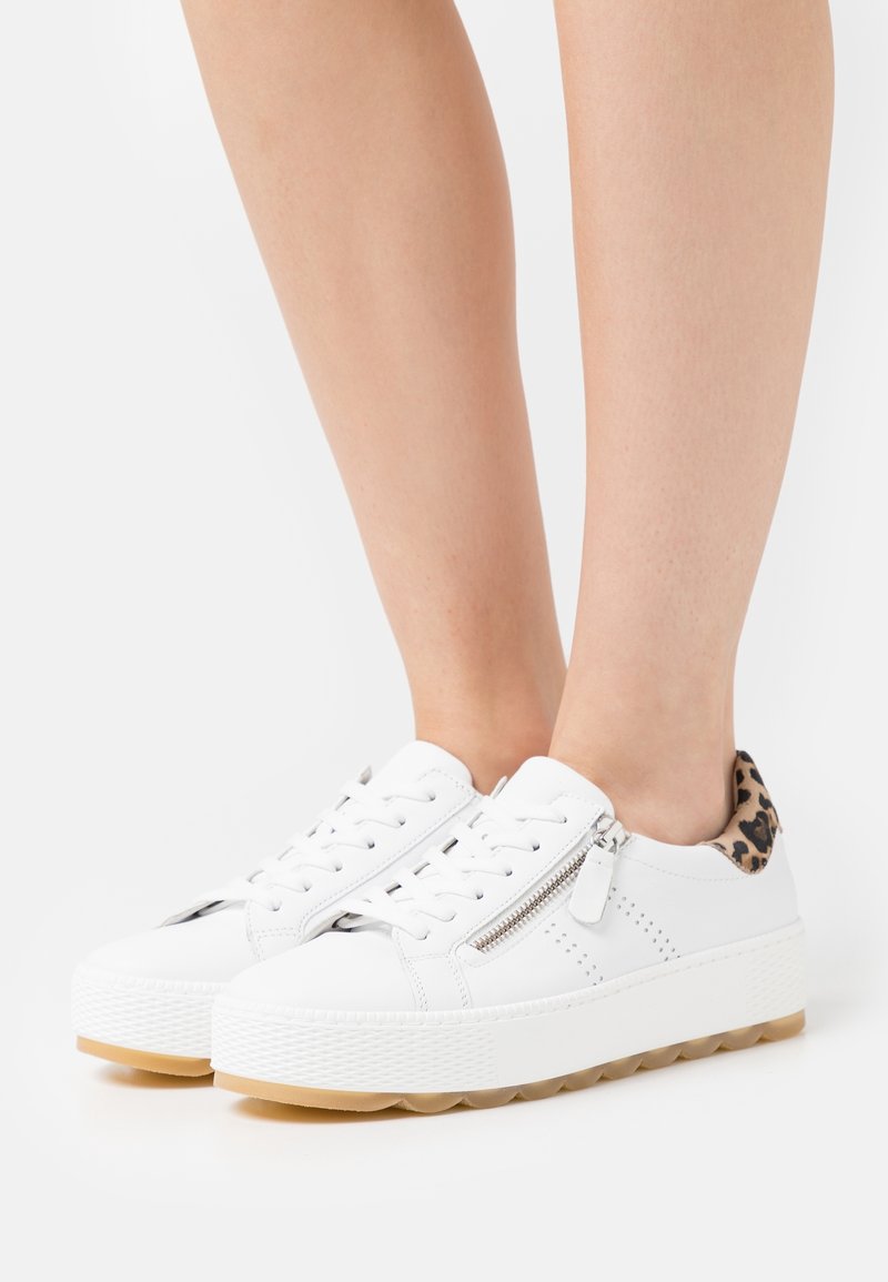Baskets blanches avec un dessus en cuir lisse, des détails perforés, une fermeture éclair sur le côté et un accent en imprimé léopard au talon. Semelle en caoutchouc.