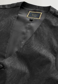 Fekete mellény paisley mintával, texturált anyaggal, selymes béléssel és egy gombos záródással. A címke aranyszínű "NEXT" feliratot visel.