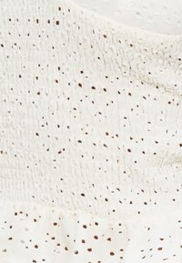 Gros plan sur un tissu blanc avec une texture smockée et de petits œillets régulièrement espacés, disposés selon un motif en grille.