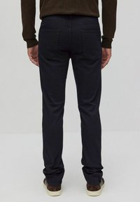 Mörkblå jeans med rak benform, med två bakfickor och en jämn, texturerad yta. Bärs med bruna skor.