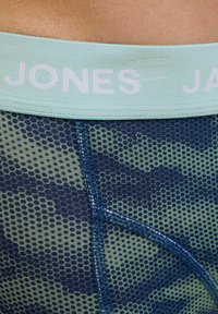 Boxerii bărbați cu o bandă de talie mint deschisă etichetată "JONES". Materialul are un model de fagure verde și bleumarin, cu detalii de cusătură în contrast.