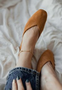 Bailarinas de ante en color marrón claro con punta afilada y corte en forma de V. Combinadas con jeans oscuros y un tobillo con pulsera decorativa de pequeñas cuentas.