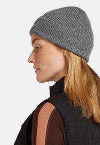 Gray knit beanie with ribbed texture. The hat sits snugly on the head, complementing the black vest and brown top with orange accents.