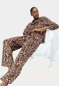 Set pyžam s leopardím potiskem vyrobený z měkké látky, s košilí na knoflíky a dlouhými kalhotami, v uvolněném střihu a s jemným leskem.