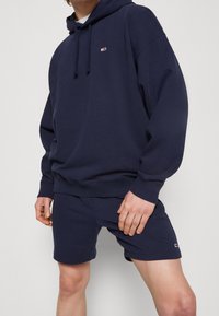 Navy hoodie och shorts set gjort av mjuk bomull. Har en framficka, dragsko på huva och logotypdetaljer på båda plaggen.