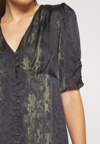 Dark green and black patterned dress with a V-neck, puffed sleeves, and button details along the front, featuring a smooth, silky texture.