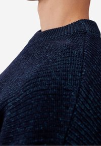 Suéter de punto azul oscuro con un patrón texturizado, que presenta un cuello acanalado y costuras de hombro en ángulo. La vista en primer plano muestra el detalle del material.