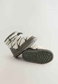 Gray plush ankle boots with a fluffy white upper featuring black stripes, thick rubber soles with textured grip, and a pull tab at the back.