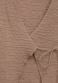 Texturerad, taupe-tyg med en rynkad yta. Har en V-ringning och en knytning med ett tunt, matchande snöre.