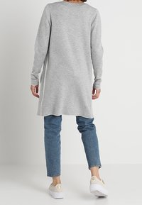 Grå tröja klänning med långa ärmar och rund halsringning, med en längd vid mitten av låren och subtila sidoklister. Bärs med blå jeans och ljusa sneakers.