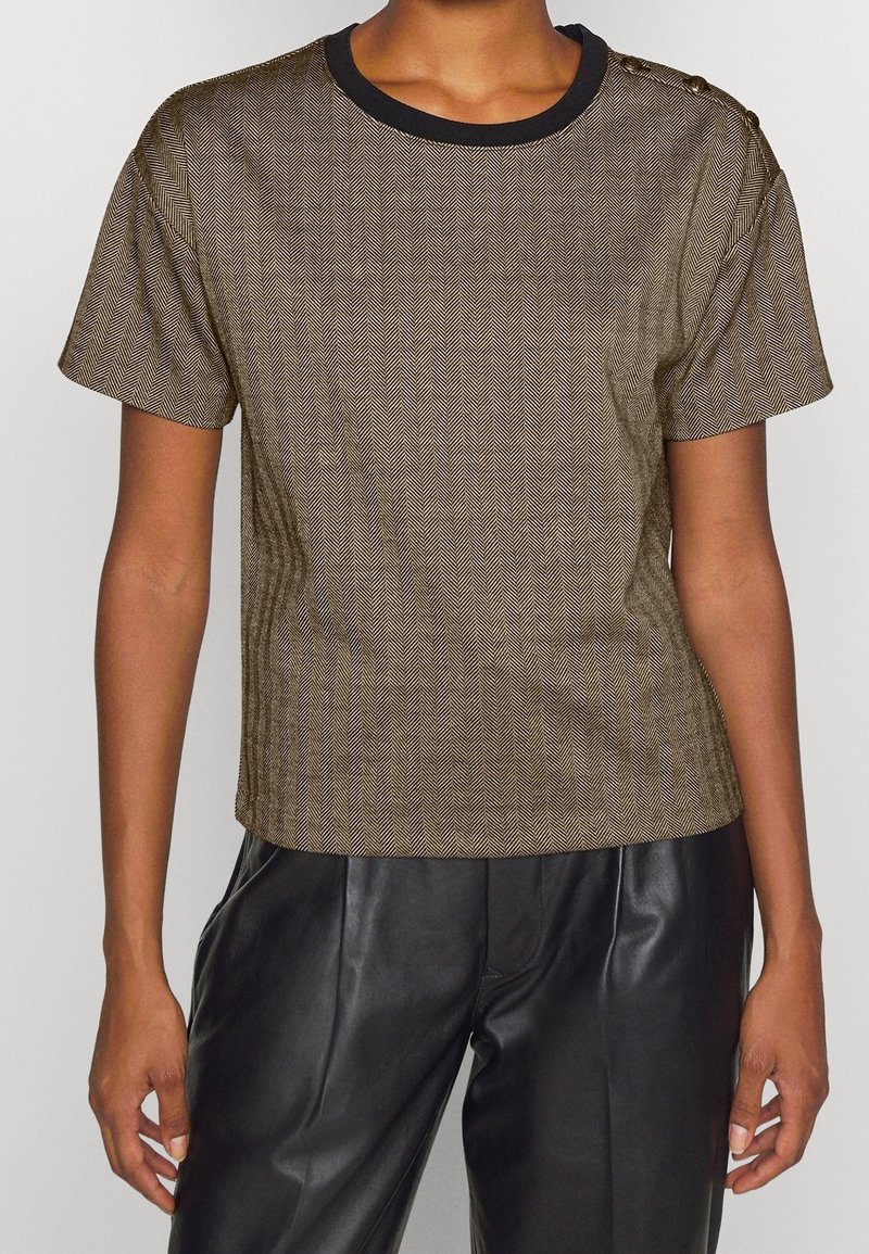 Brun herringbone-mönstrad kortärmad topp med svart rund halsringning och knappdetaljer på ena axeln, matchat med svarta läderbyxor.