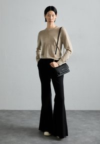 Beige gebreide trui, zwarte flared broek, zwarte schoudertas met gouden ketting. Glad textuur, aansluitend om de taille, los bij de benen.