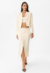 Geknipte crèmekleurige blazer met knopen, bijpassende rok van gemiddelde lengte met een voorknijp, gecombineerd met zwarte open teen hakken. Gladde stof en perfecte pasvorm.