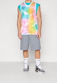 Jersey sin mangas colorido con un patrón de acuarela en rosa, amarillo y verde, combinado con pantalones cortos grises y zapatillas deportivas negras.