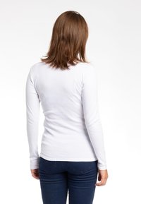Camicia bianca a maniche lunghe in tessuto morbido, design aderente, superficie liscia, abbinata a jeans in denim scuri, vista da dietro.