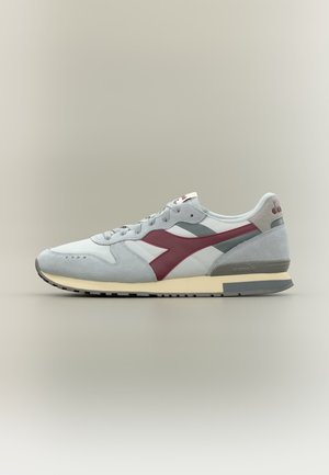 Baskets gris clair et blanc avec logo latéral bordeaux, accents gris, semelle crème et fermeture à lacets sur fond neutre.