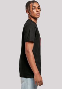 Black cotton t-shirt featuring a crew neckline, short sleeves, and a printed design on the front. Worn with light blue jeans.