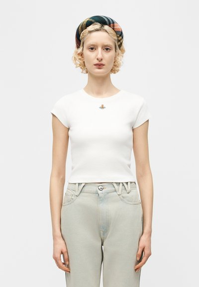Ξανθός/ή που φοράει ένα λευκό εφαρμοστό cropped t-shirt με ένα μικρό πολύχρωμο λογότυπο, καρό κορδέλα για τα μαλλιά και ανοιχτόχρωμο τζιν ψηλόμεσο.
