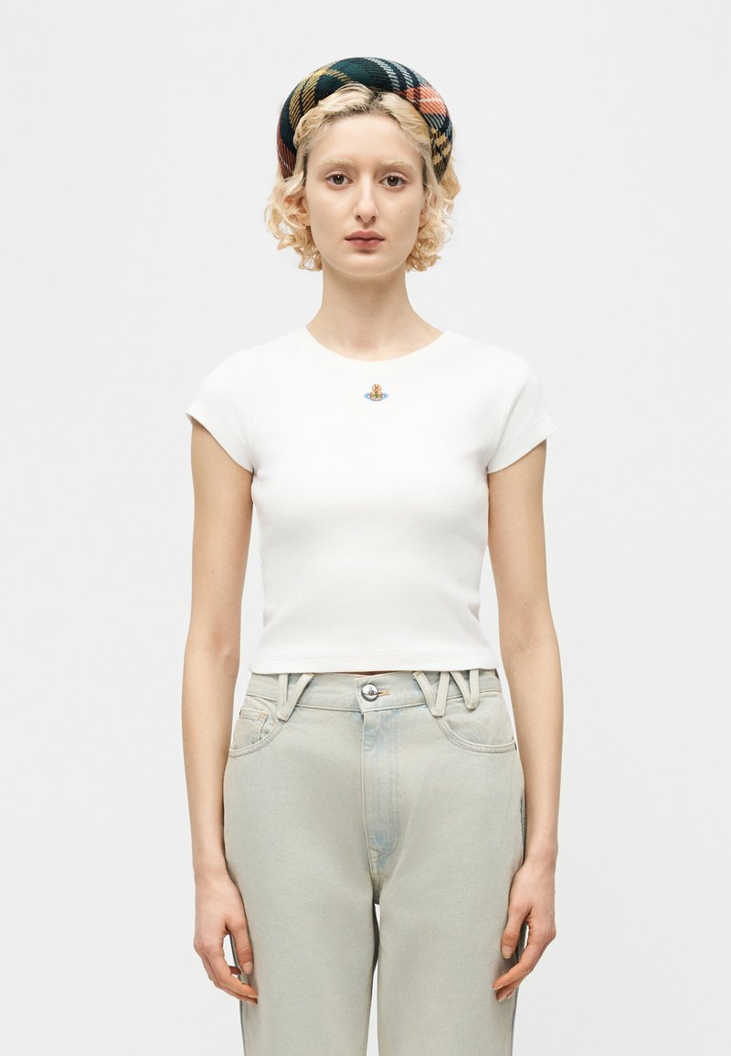 Ξανθός/ή που φοράει ένα λευκό εφαρμοστό cropped t-shirt με ένα μικρό πολύχρωμο λογότυπο, καρό κορδέλα για τα μαλλιά και ανοιχτόχρωμο τζιν ψηλόμεσο.