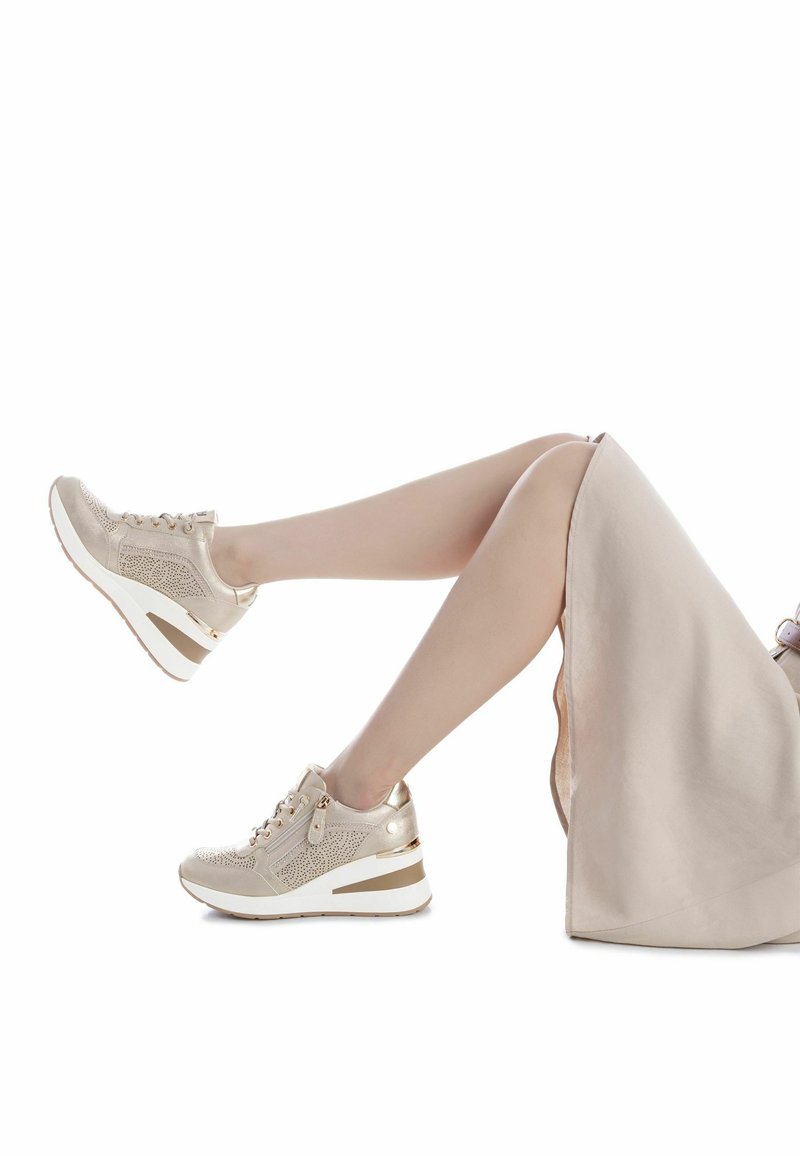 Zapatillas beige con un detalle metálico dorado, diseño perforado, cierre con cordones y tacón cuña. Suela exterior blanca.