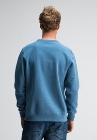 Blauwe sweatshirt van een katoenmix, met lange mouwen, ribgebreide manchetten en onderkant, ronde hals en zachte textuur; gedragen over donkerblauwe jeans.
