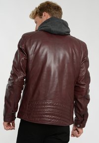 Burgunderfärgad läderjacka med texturerad finish, ruggade accenter vid midjan och axlarna samt en avtagbar grå huva.