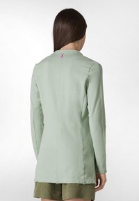 Långärmad, mintgrön topp med rund halsringning och en sömdetalj bak. Har en liten rosa etikett vid halsringningen. Slät tygtextur.