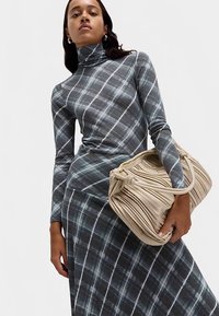Sukienka z golfem w szarym kolorze z kratkowanym wzorem; posiada dopasowaną sylwetkę oraz plisowaną beżową torebkę o zaokrąglonym kształcie z złotymi akcentami.