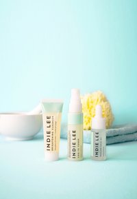 Kolme ihonhoitotuotetta: valkoinen tuubi, vaaleanvihreä pullo ja kirkas pipettipullo, aseteltuna vaaleansinisen taustan ja pyyhkeen päälle.