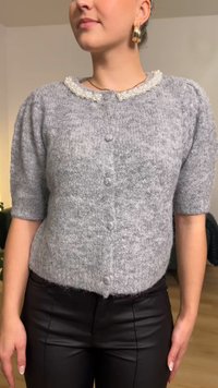 Siv pleten pulover s kratkimi rokavi, ovratnik okrašen z biseri in zapiranjem na gumbe. Mehka tekstura, rahlo ohlapna oblika.